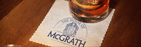 Glass of whiskey with a lemon wedge on a napkin with 'The House of McGrath' logo.