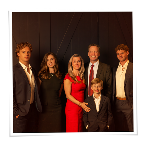 A family portrait of six people posing together against a dark paneled background