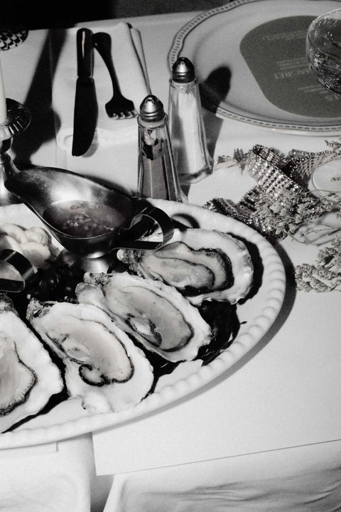 Black and white photograph of a seafood platter featuring raw oysters on a white table setting with salt and pepper shakers.