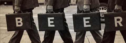 Four people in dark suits walk forward carrying black briefcases that spell out the word 'BEER'