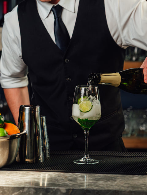 Bartender pouring a drink into a glass with ice and lime garnish.