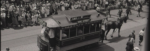 Vintage streetcar being pulled by horses on a city street with pedestrians in the background